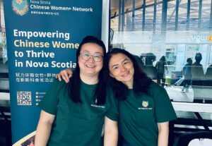Two women in matching NSCWN t-shirts pose beside the network's banner at the Wellness Expo.