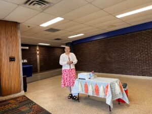 Ellie stands beside a decorated table indoors, next to a cooler and printer.