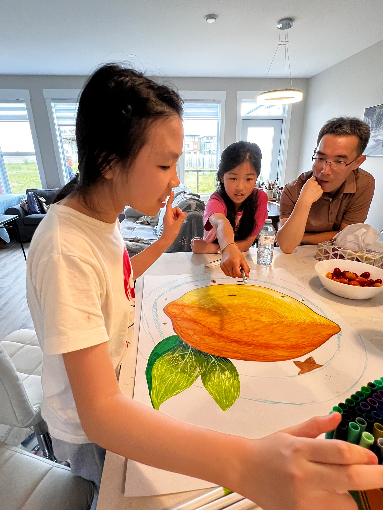 Two children and a man look over a finished lemon poster on a kitchen table.