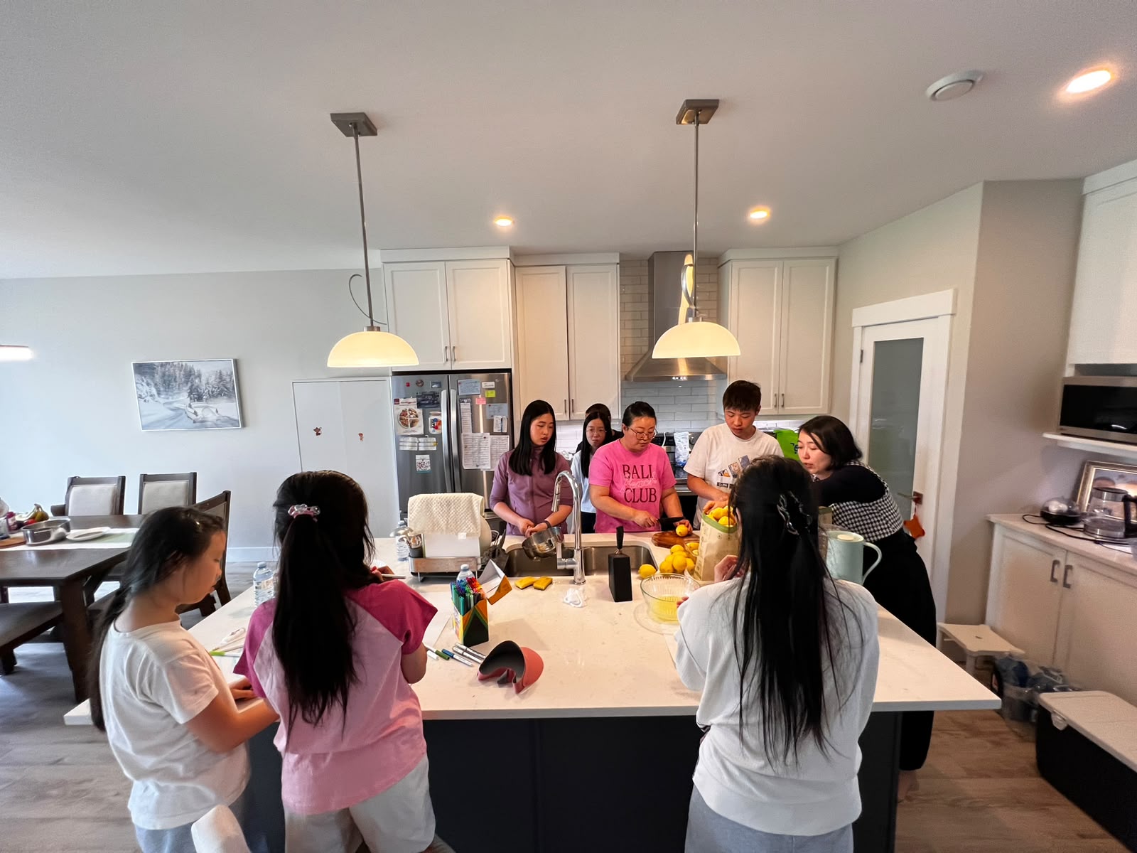 A group gathers around a kitchen island preparing lemons and supplies for a lemonade stand.