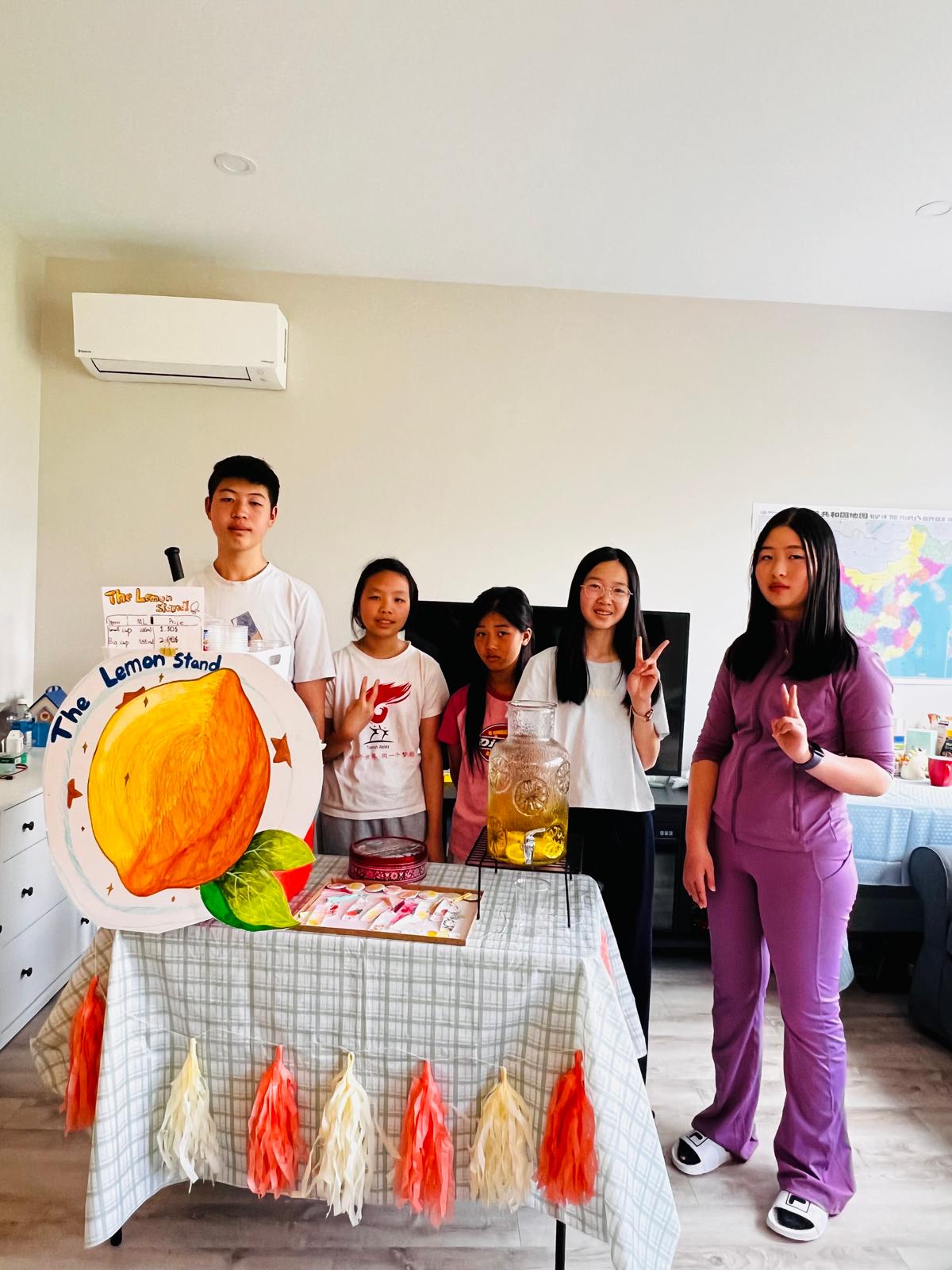 Five participants pose behind the decorated lemonade stand table before heading out.