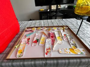 A tray displays handmade bookmarks and buttons with summer and lemonade-themed designs.