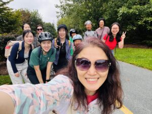 Large group poses for a selfie on a paved trail surrounded by trees