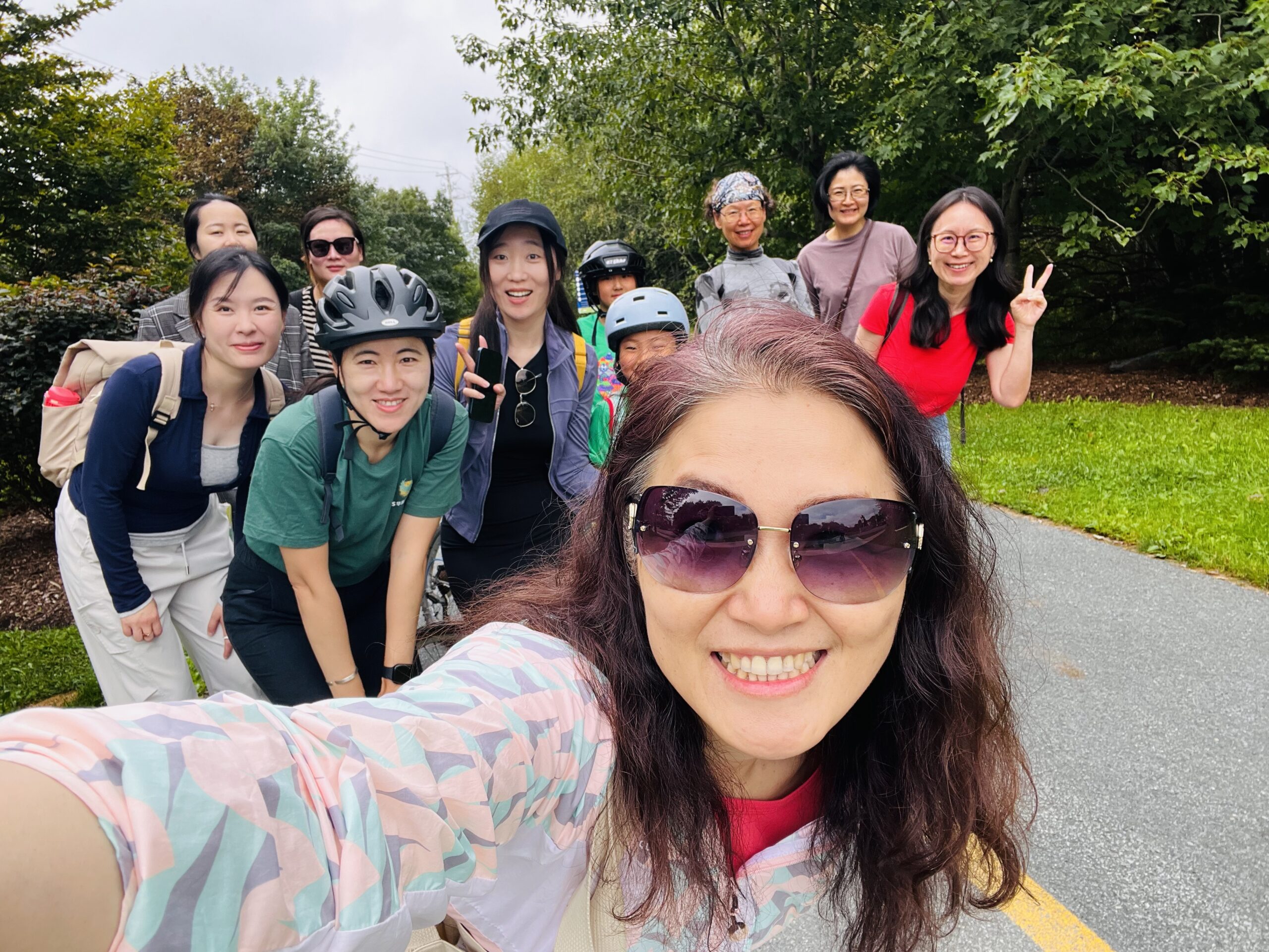 Large group poses for a selfie on a paved trail surrounded by trees